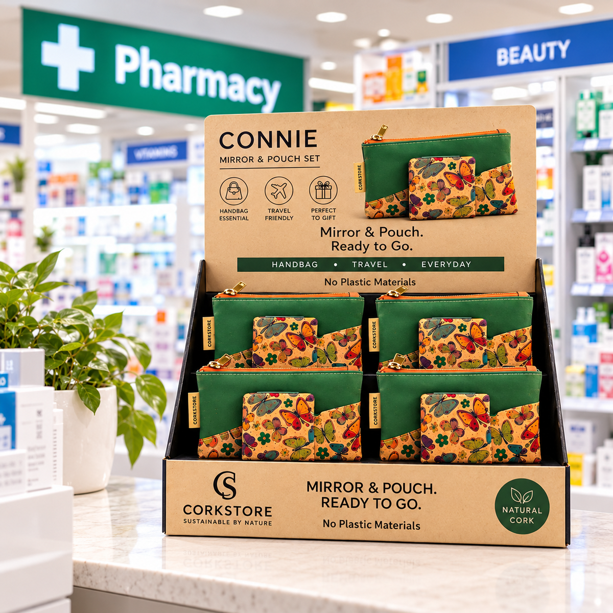 A retail display box of Corkstore Connie Mirror & Pouch Set, showing multiple green and floral patterned zip pouches with mirrors inside a cardboard stand, set in a pharmacy store environment.